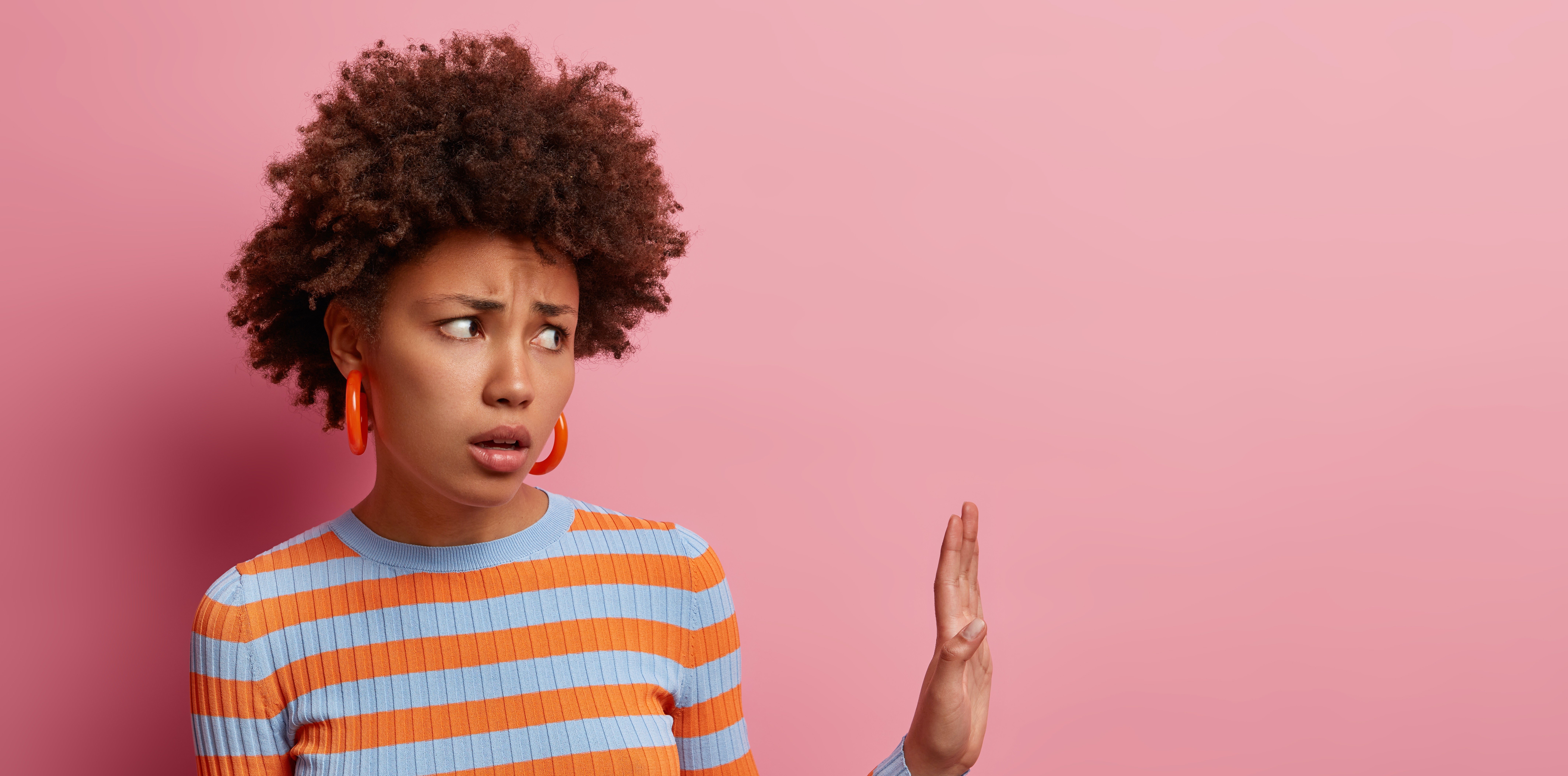 discontent-african-american-woman-keeps-palm-refusal-gesture-says-stays-away-from-me-come-closer-avoids-crowded-places-grimaces-disappointed-isolated-pink-wall-empty-space
