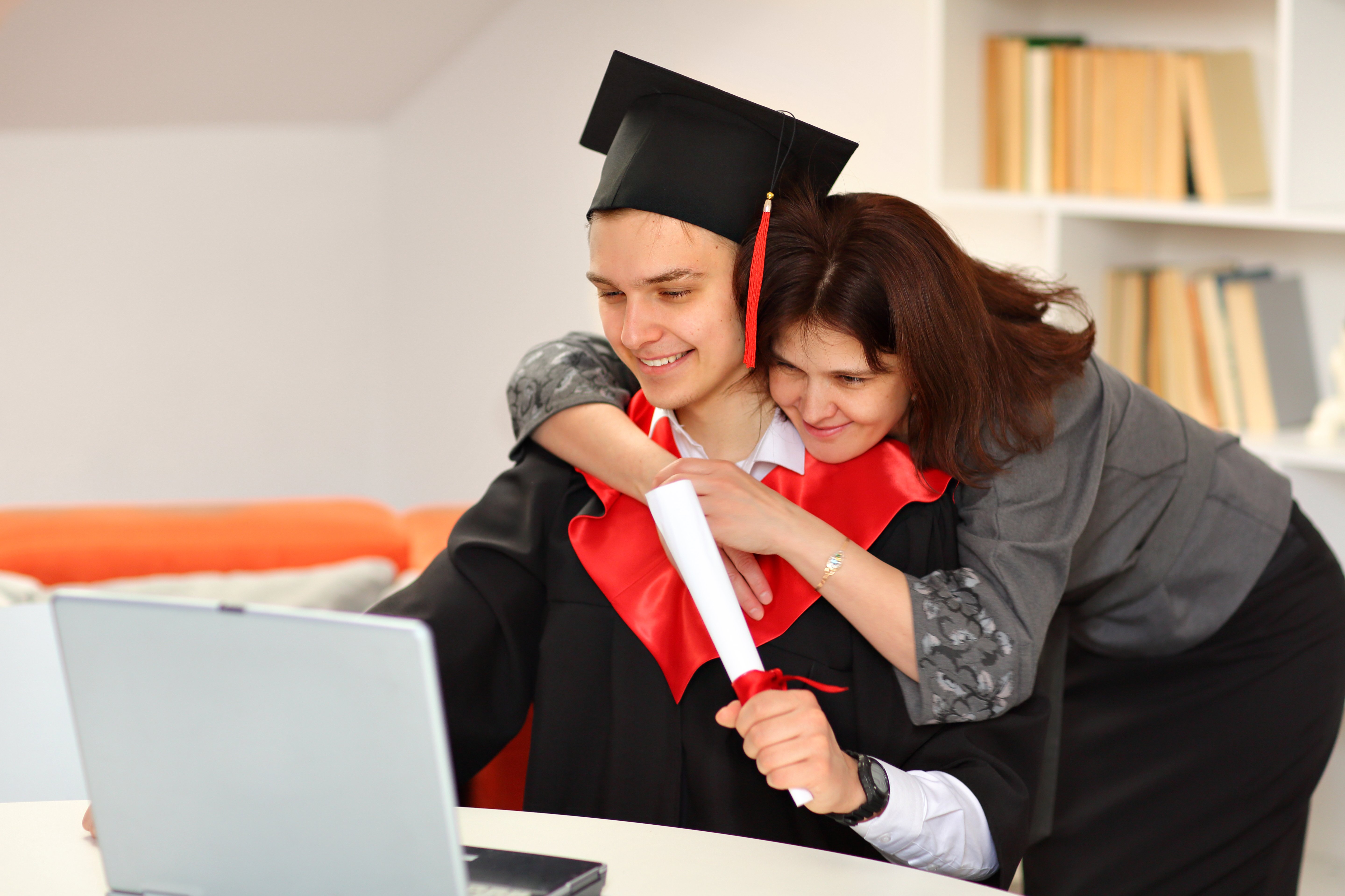 mother-hugs-her-son-student-graduation-gown-graduate-cap-holds-scroll-his-hand-watches-broadcast-graduation-ceremony-while-home